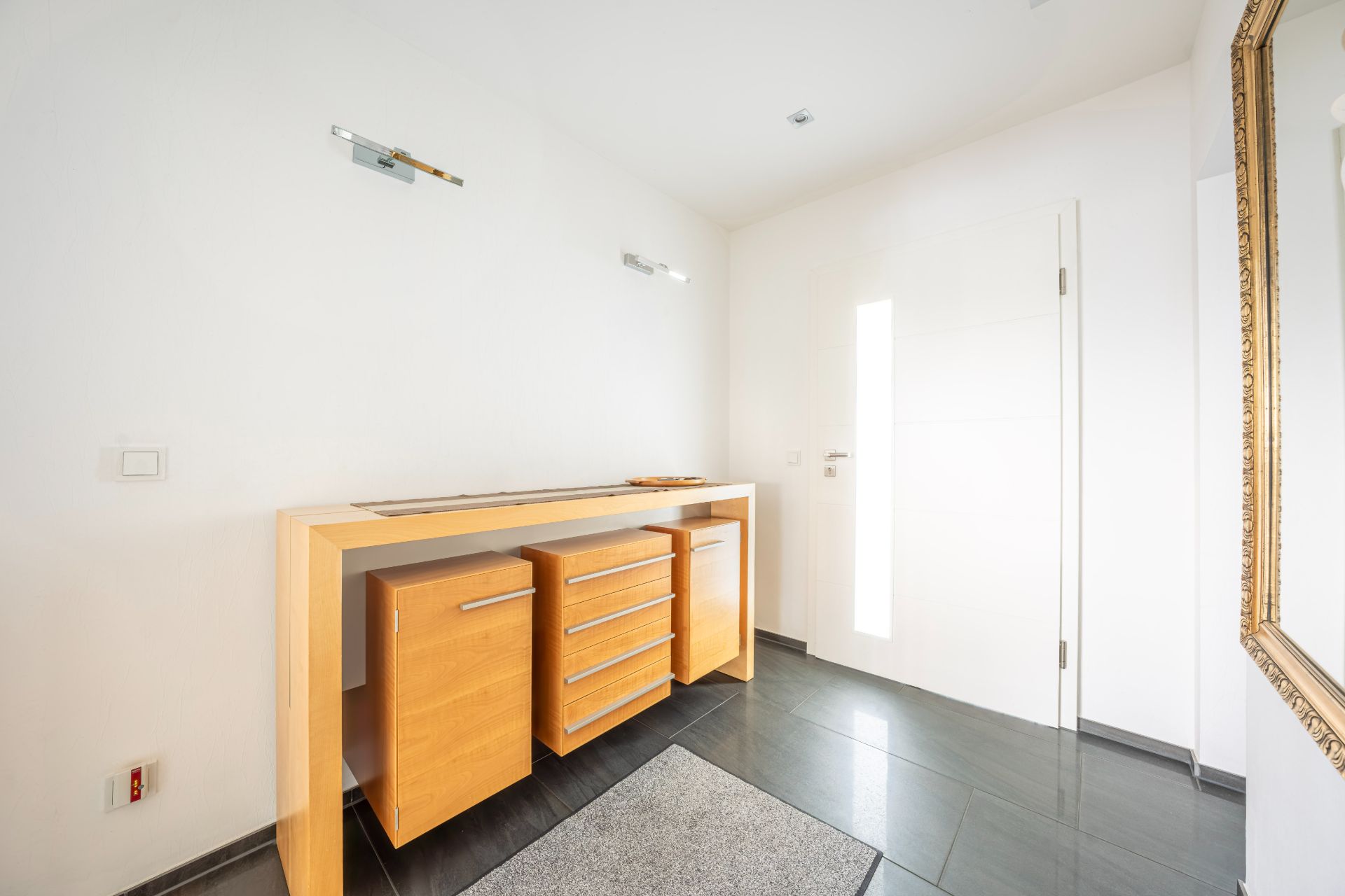 Heller Flur mit Holzmöbel, grauem Teppich und großem Spiegel an der Wand.