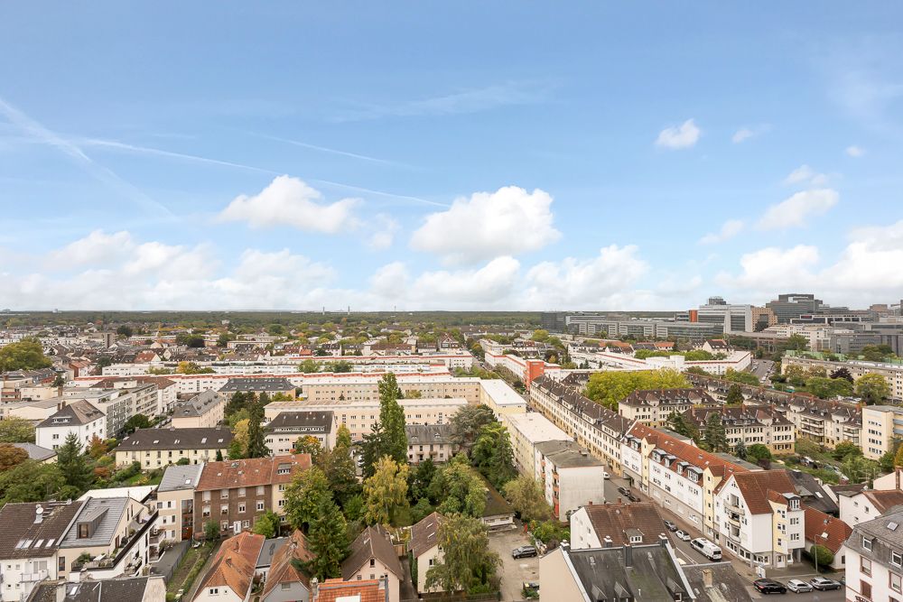 Blick über ein Wohngebiet mit vielen Häusern und Bäumen unter blauem Himmel mit Wolken.
