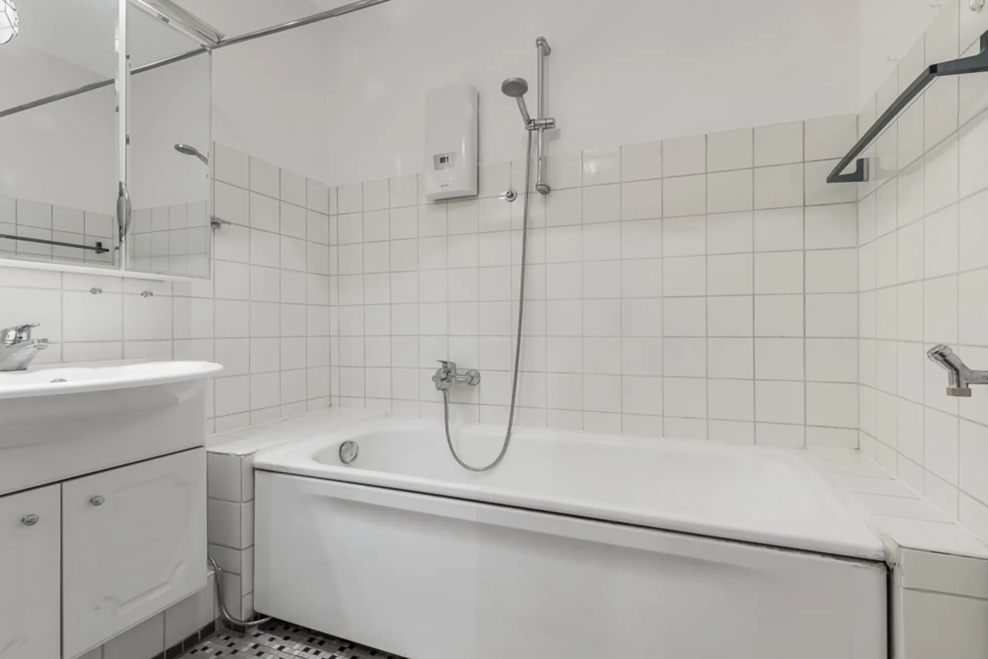 Weiß gefliestes Badezimmer mit Badewanne, Spiegel, Waschbecken und Duschkopf.
