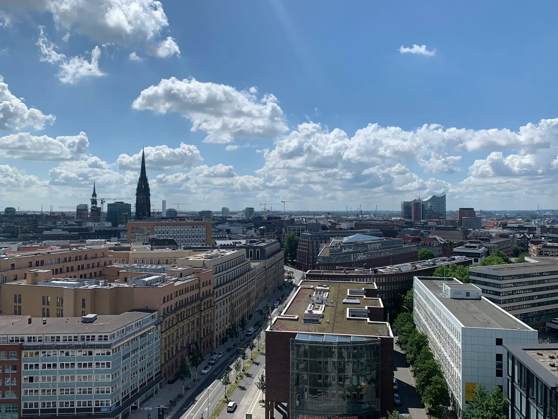 Stadtansicht mit vielen Gebäuden, einer Kirche mit hohem Turm und blauem Himmel mit Wolken.