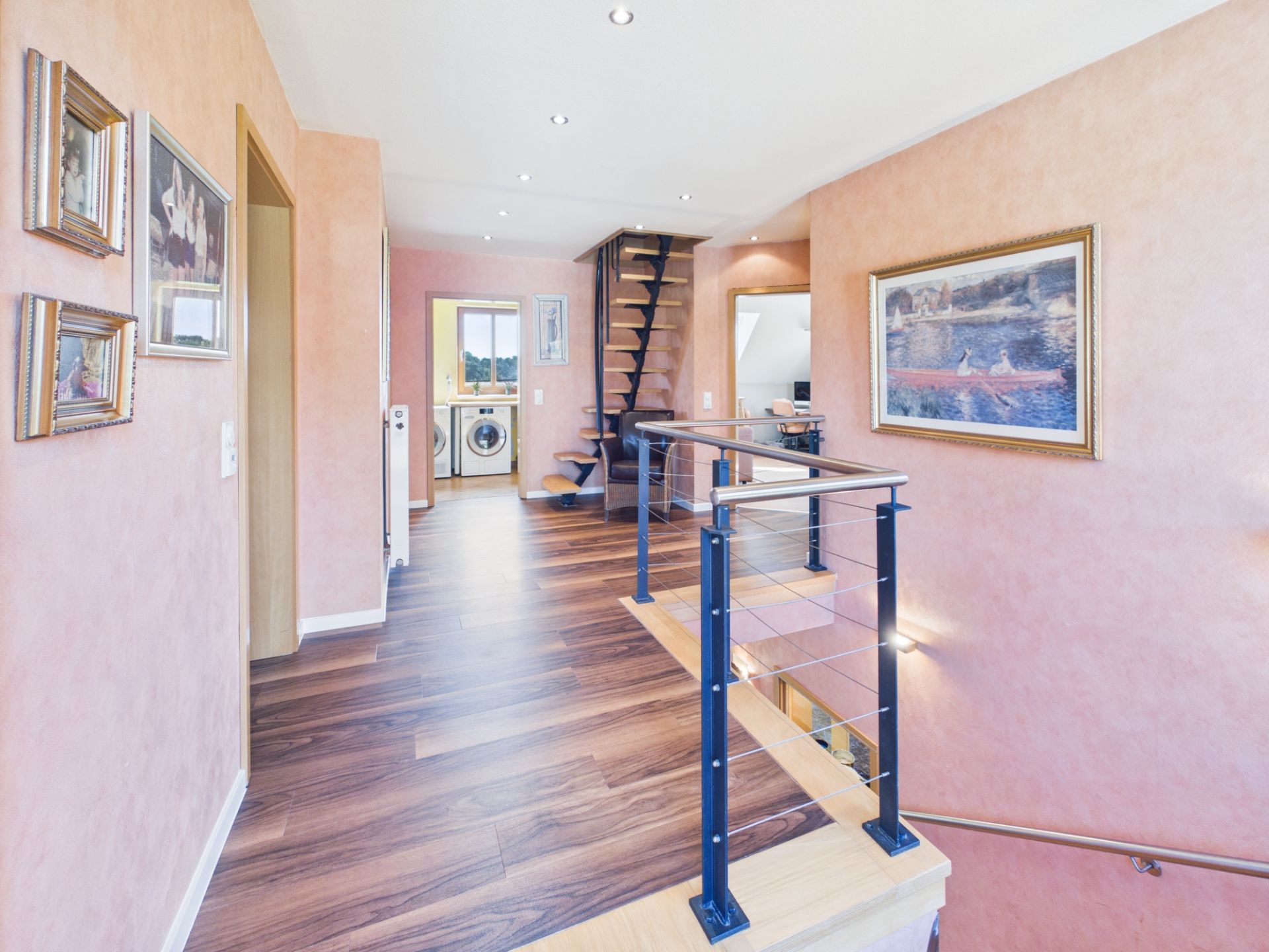Heller Flur mit Holzboden, Treppe, Wandbildern und Blick auf eine Waschküche.