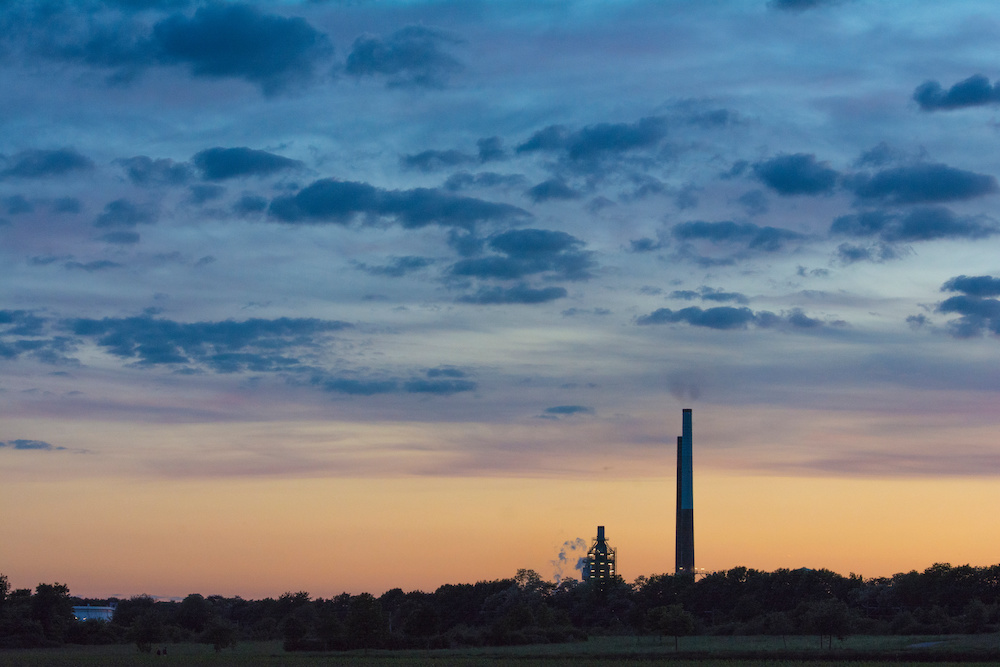 Industrieanlage mit Schornstein vor einem bunten Himmel bei Sonnenuntergang.