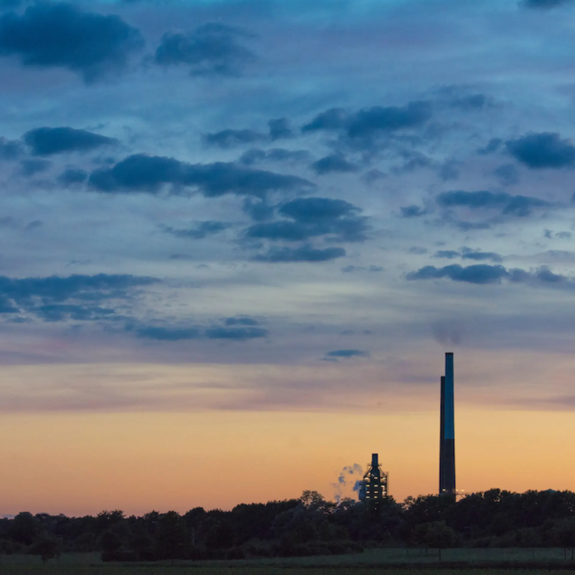 Industrieanlage mit Schornstein vor einem bunten Himmel bei Sonnenuntergang.