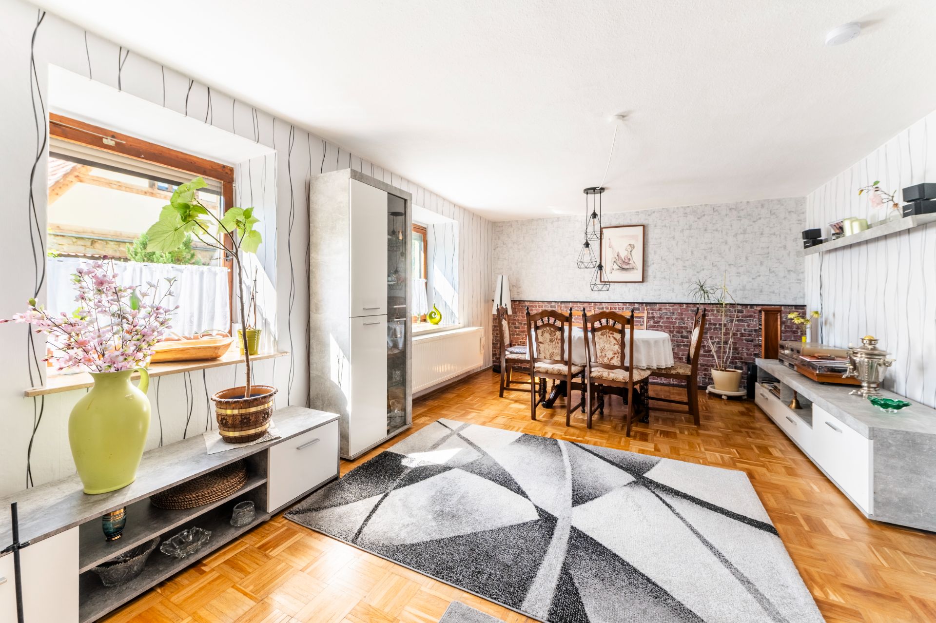 Helles Wohnzimmer mit Holzboden, Esstisch, Sideboards, Teppich und großen Fenstern.