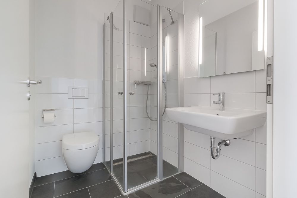 Modernes Bad mit Dusche, Wandtoilette, Waschbecken und Spiegel, weiße Fliesen.