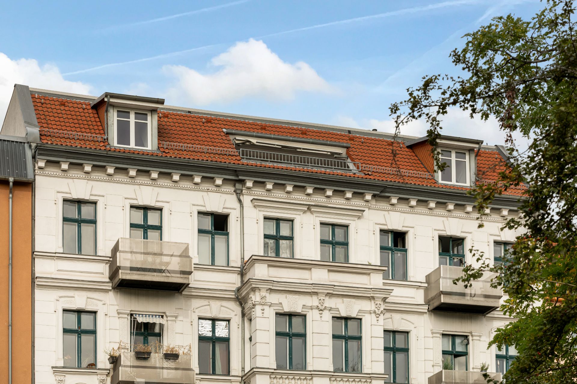 Fassade eines mehrstöckigen Wohnhauses mit Balkonen und roten Dachziegeln.