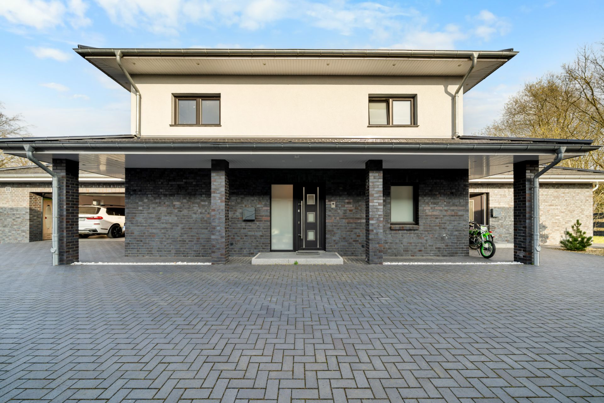 Moderne zweistöckige Hausfassade mit dunklen Klinkersteinen, breitem Eingang und großer Einfahrt.