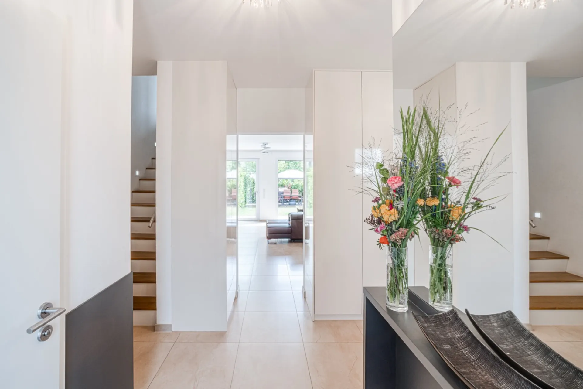 Heller Flur mit zwei Treppen, einer Blumenvasen und Blick ins Wohnzimmer.