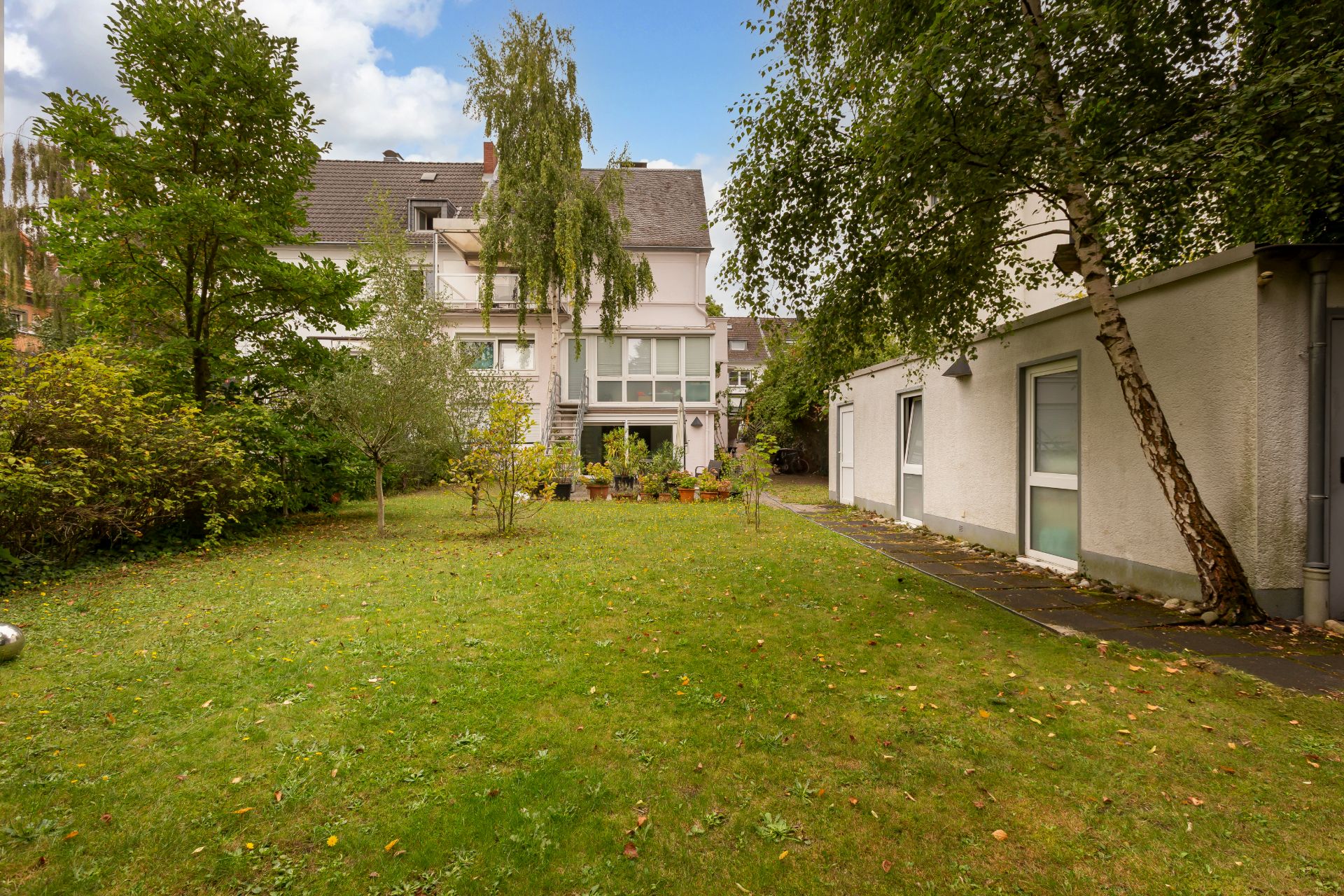 Grüner Garten mit Rasen, Bäumen und Sträuchern vor einem Wohnhaus und Anbau.