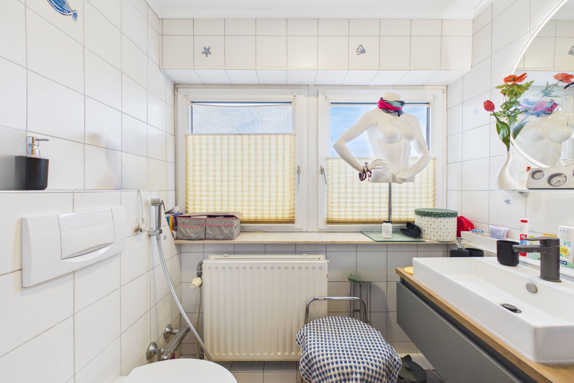 Kleines Badezimmer mit WC, Waschbecken, zwei Fenstern und Deko-Objekten auf der Fensterbank.