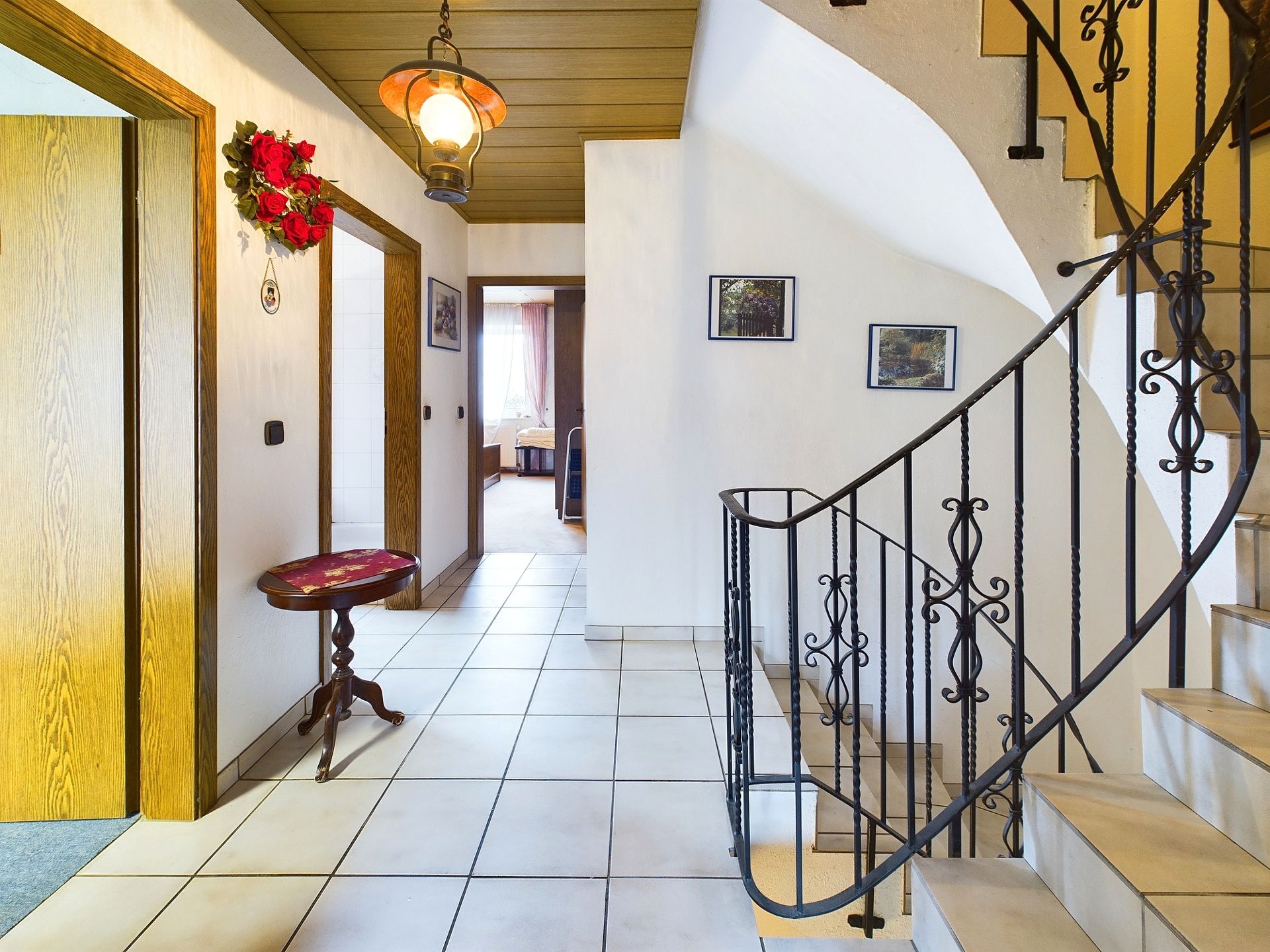 Flur mit Treppe, kleinen Tisch, Wandbildern und heller Fliese im Wohnhaus.