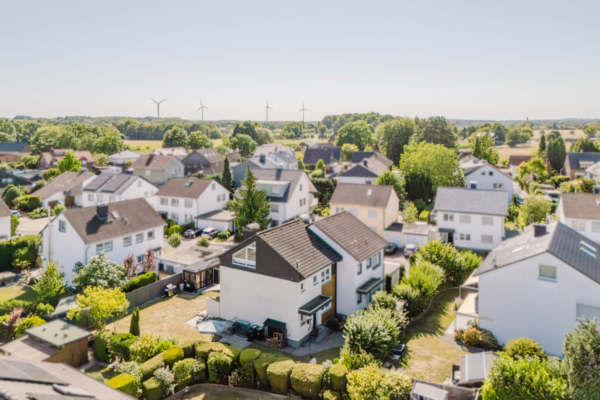 Luftaufnahme von mehreren Einfamilienhäusern mit Gärten in einer grünen Wohnsiedlung.