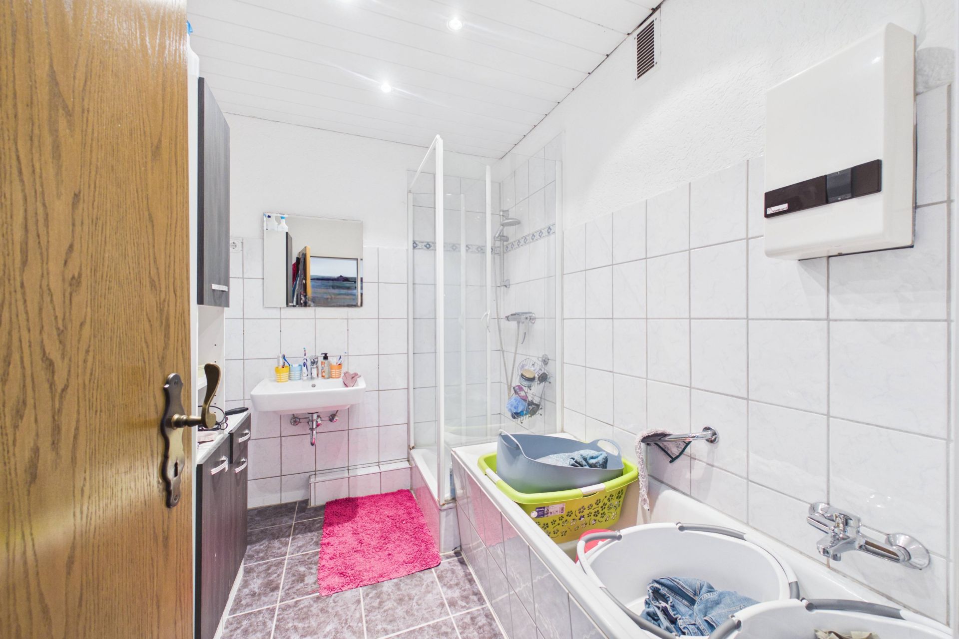Helles Badezimmer mit Badewanne, Dusche, Waschbecken, Spiegel und Wäschekörben.