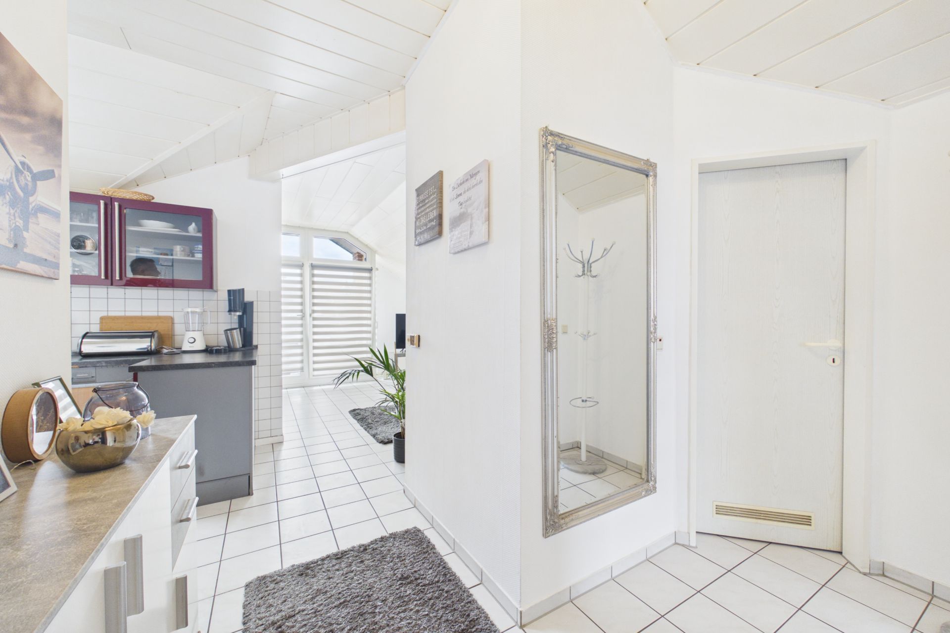 Heller Flur mit Spiegel, Teppich und Zugang zu Küche und weiterem Zimmer.