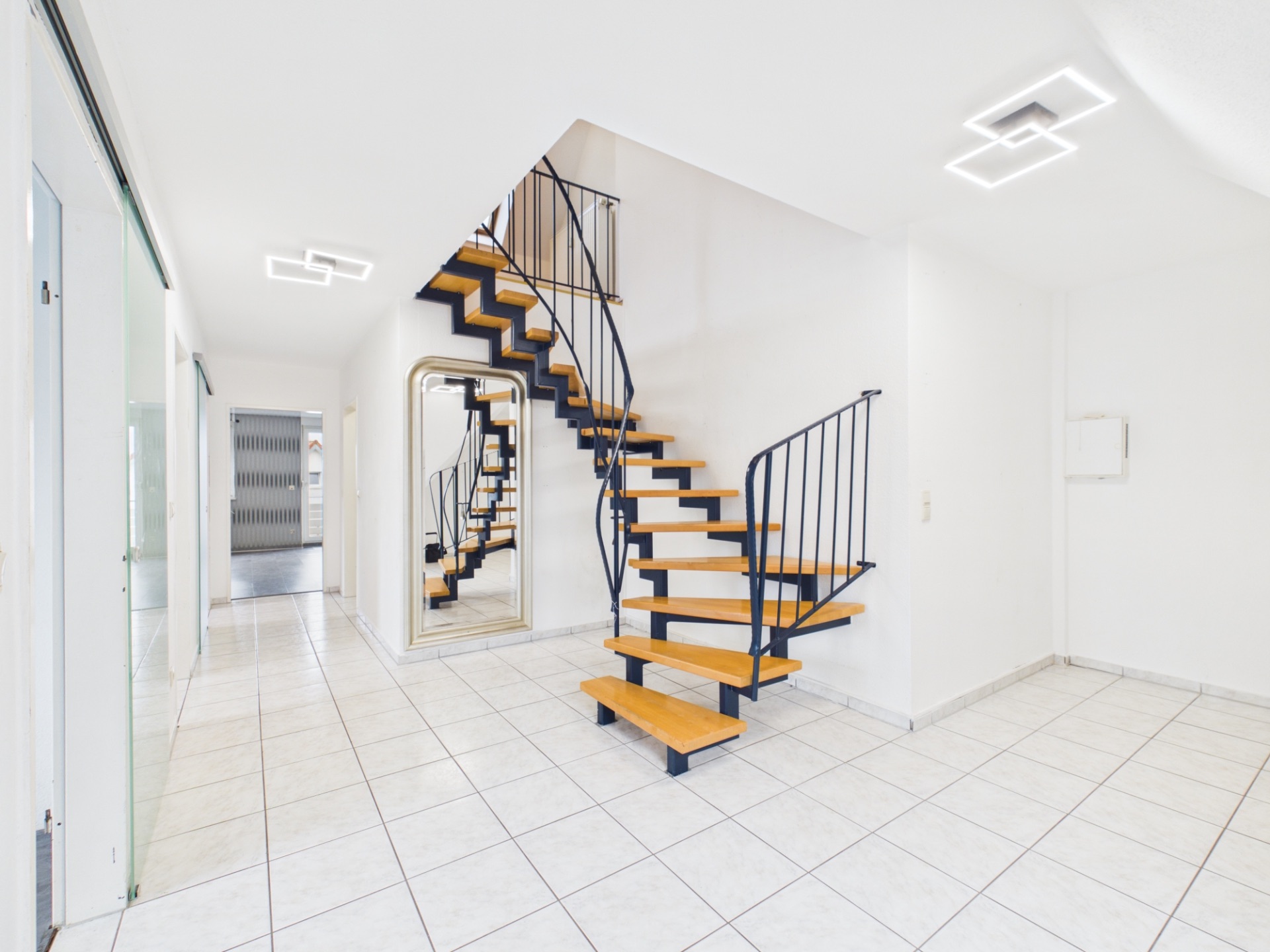 Heller Flur mit gefliesten Boden und offener Holztreppe mit schwarzem Geländer.