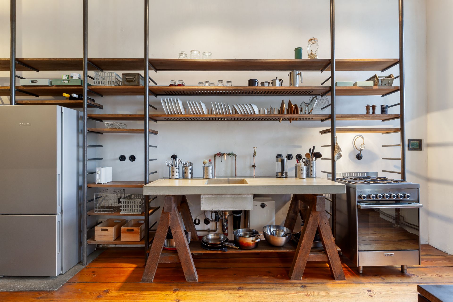 Moderne Küche mit offenem Regal, Spüle, Herd und Kühlschrank auf Holzfußboden.