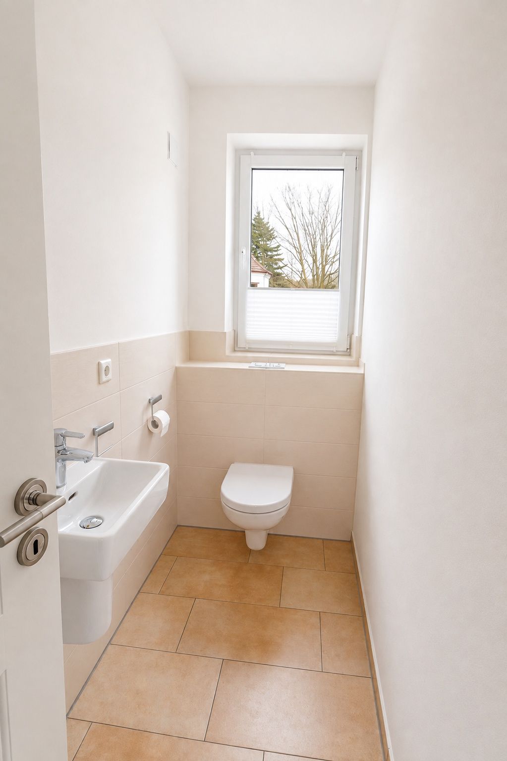 Helles Gäste-WC mit Wandtoilette, kleinem Waschbecken und Fenster.