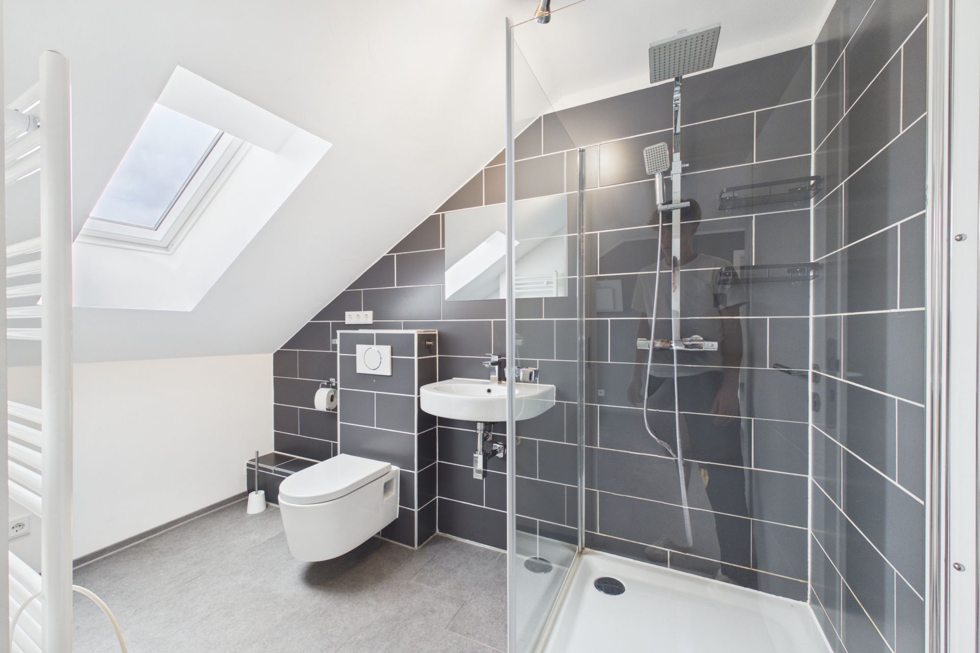 Modernes Badezimmer mit Dusche, WC, Waschbecken und Dachfenster.