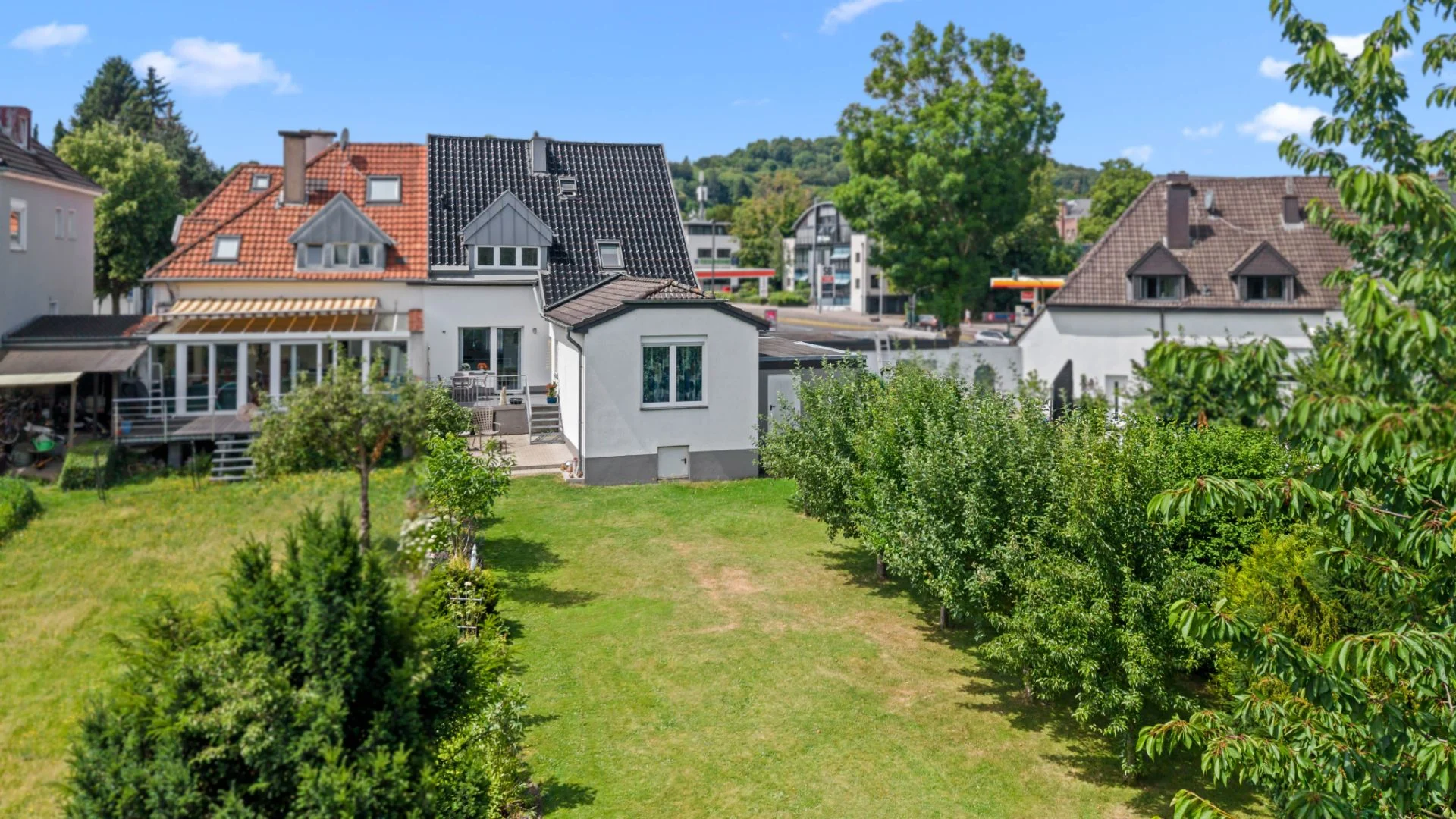 Hinteransicht eines Wohnhauses mit großer Terrasse und Garten mit Rasen und Bäumen.