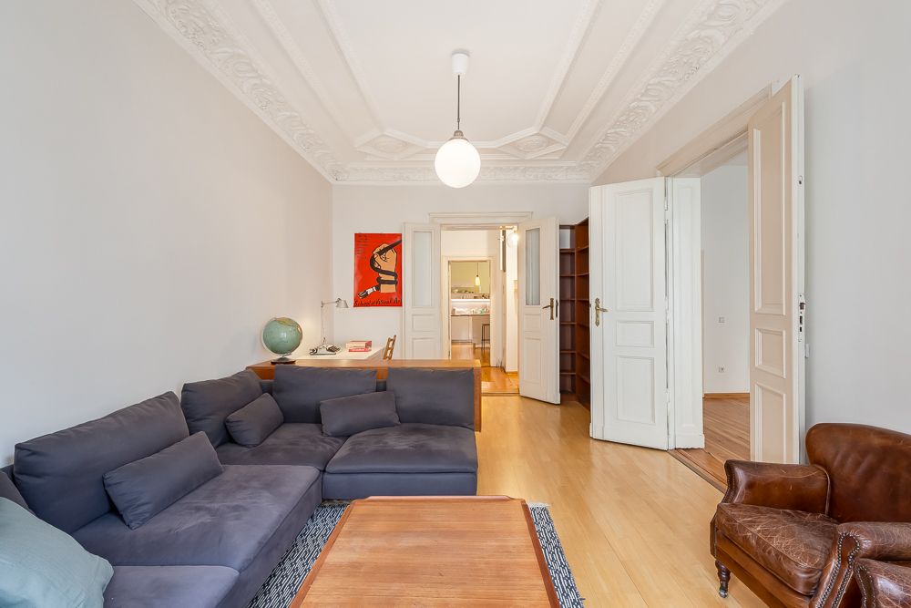 Helles Wohnzimmer mit grauem Sofa, braunem Sessel, Holztisch und Deckenleuchte.