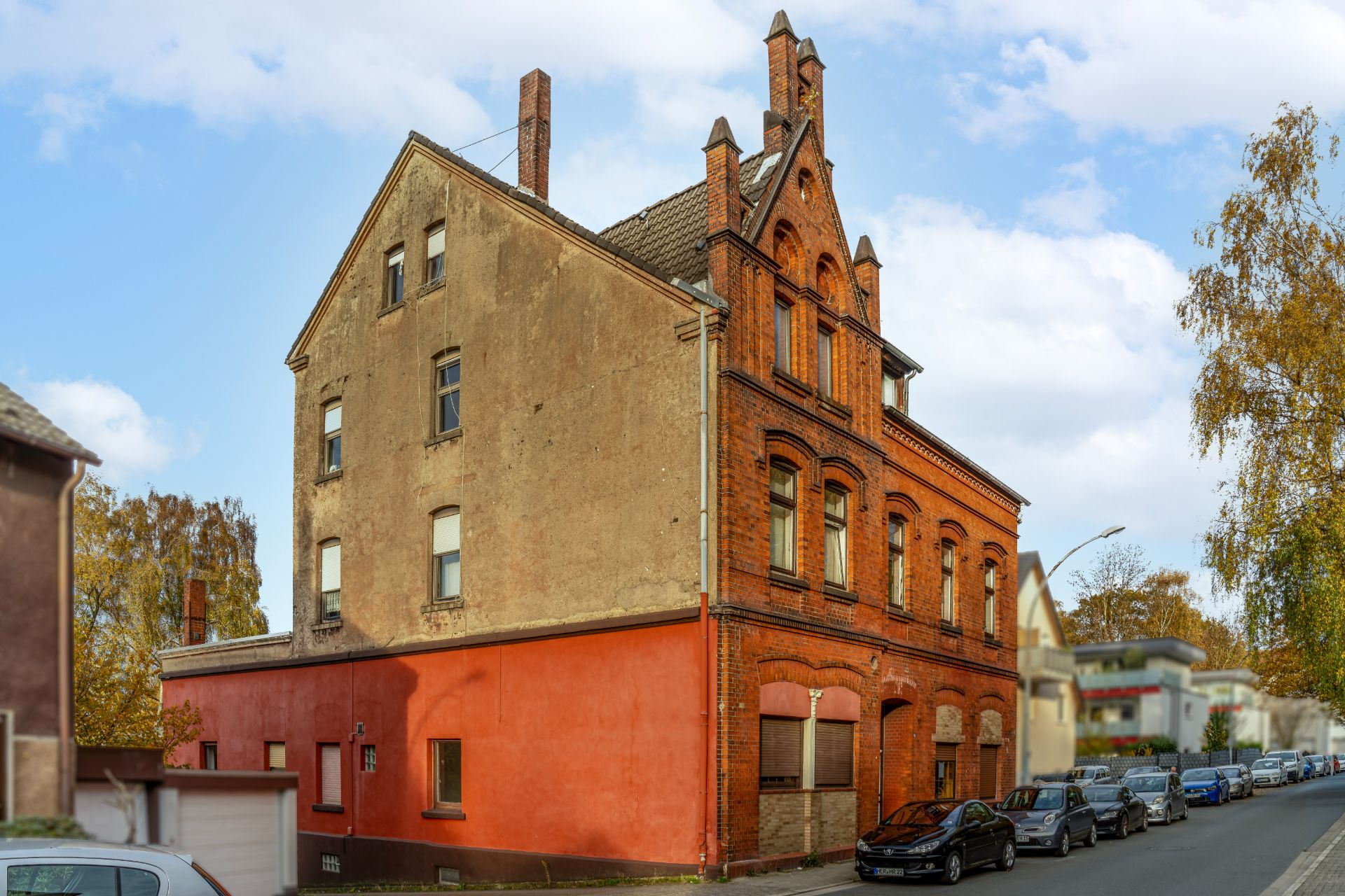Eckhaus mit roter und brauner Fassade, mehreren Fenstern und geparkten Autos an der Straße.