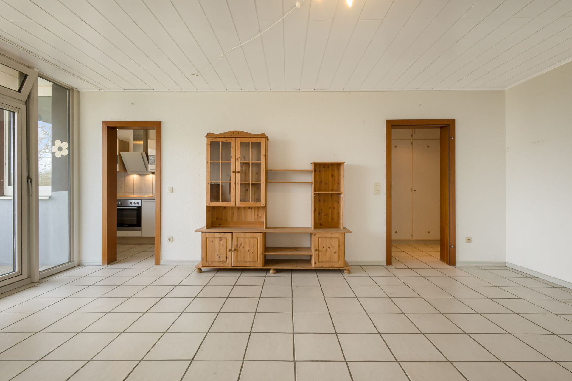 Wohnzimmer mit Fliesenboden, Holzregal, zwei Türen und Fensterfront.