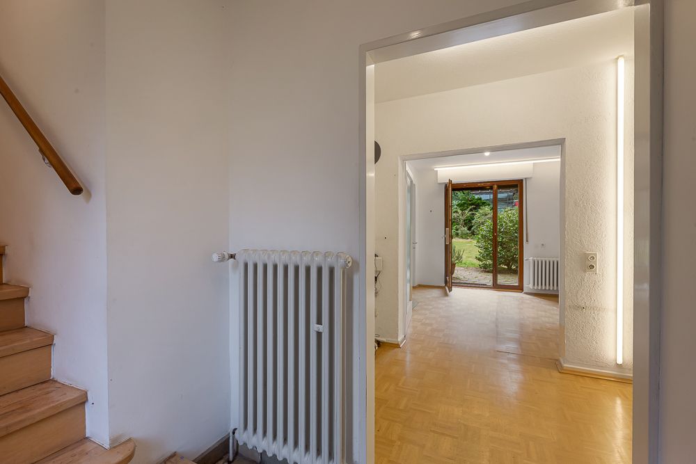 Blick vom Flur mit Treppe in ein helles Wohnzimmer mit Parkettboden und Zugang zum Garten.