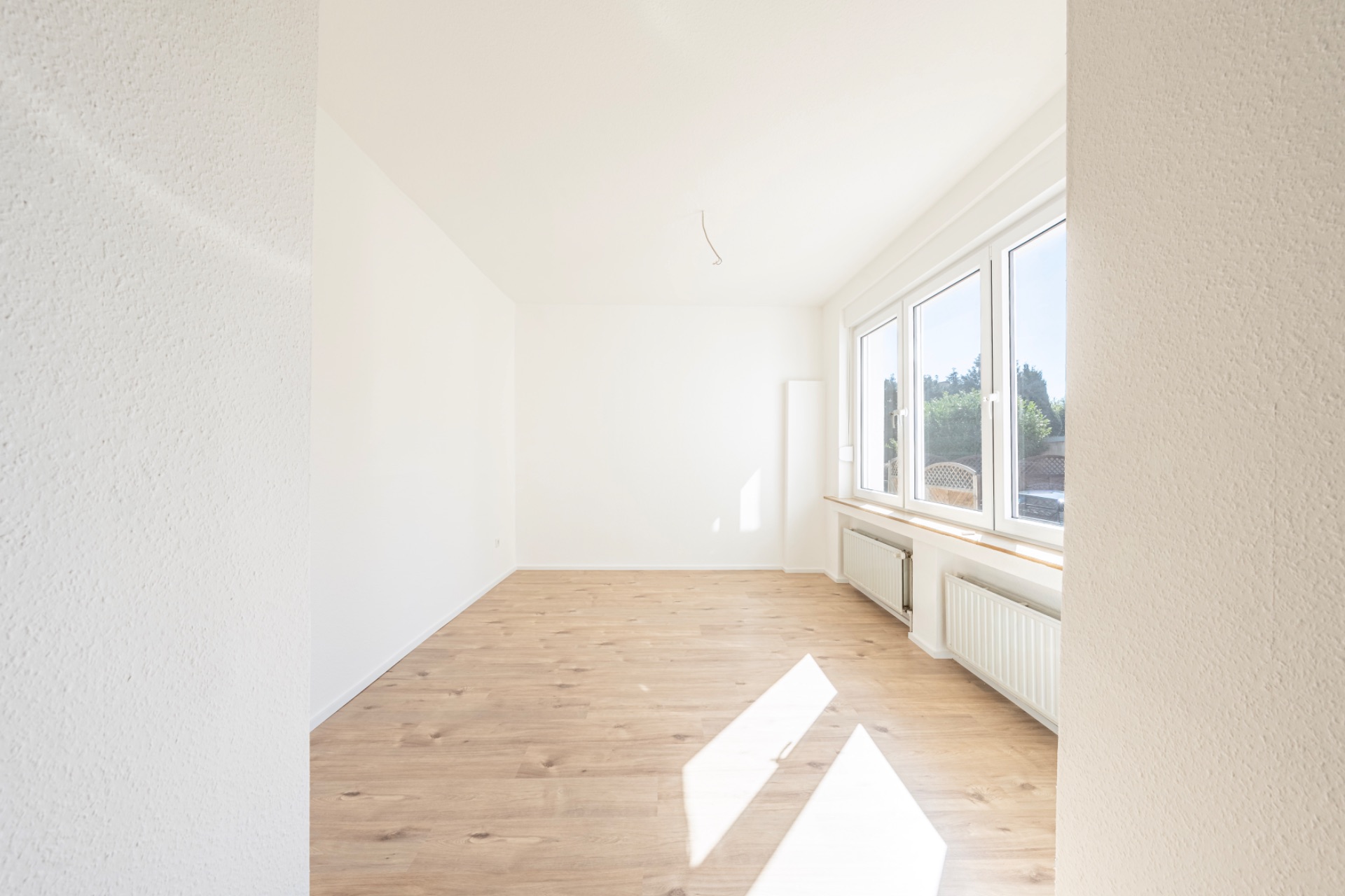 Heller, leerer Raum mit Holzfußboden und großen Fenstern an einer Seite.