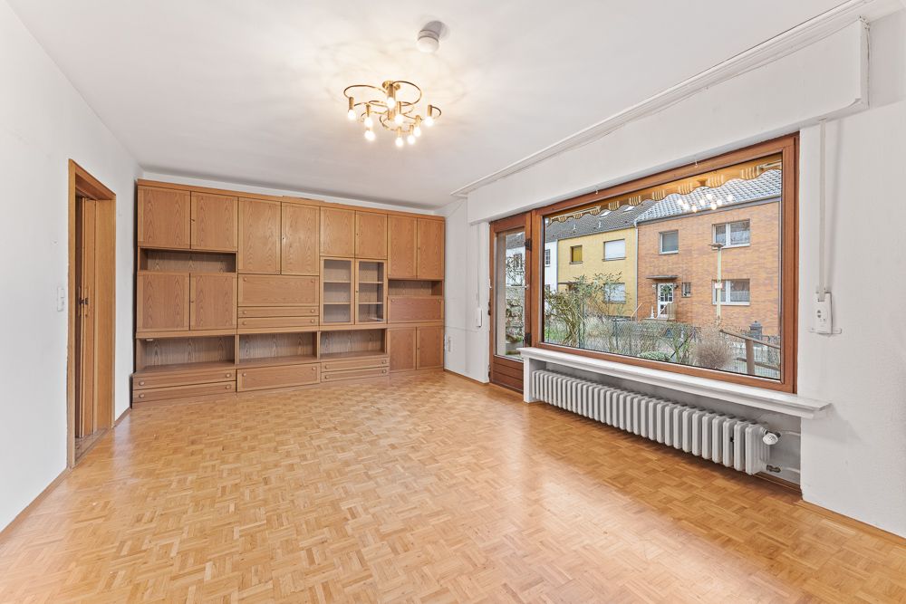 Helles Wohnzimmer mit Holzschrankwand, großem Fenster und Parkettboden.