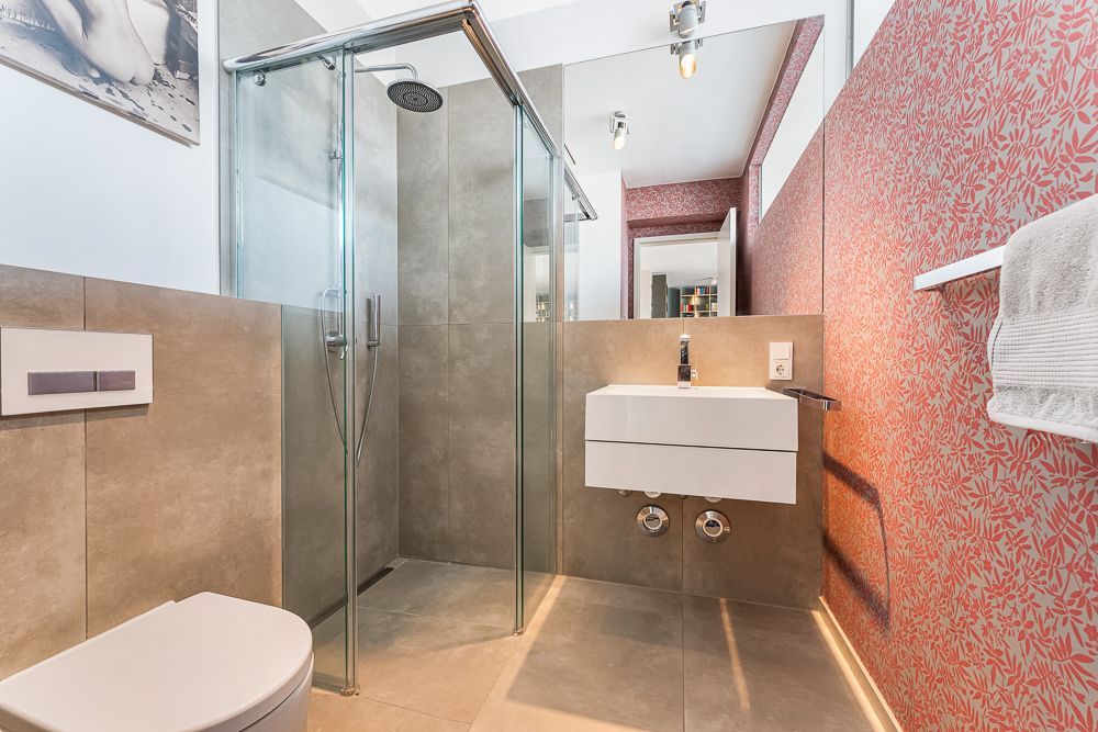 Modernes Badezimmer mit großer Dusche, Wandwaschbecken und gemusterter roten Tapete.