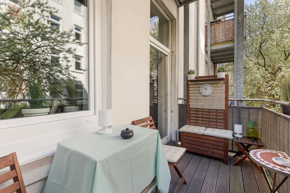 Balkon mit kleinem Tisch, zwei Stühlen und einer Sitzbank mit Uhr an der Hauswand.