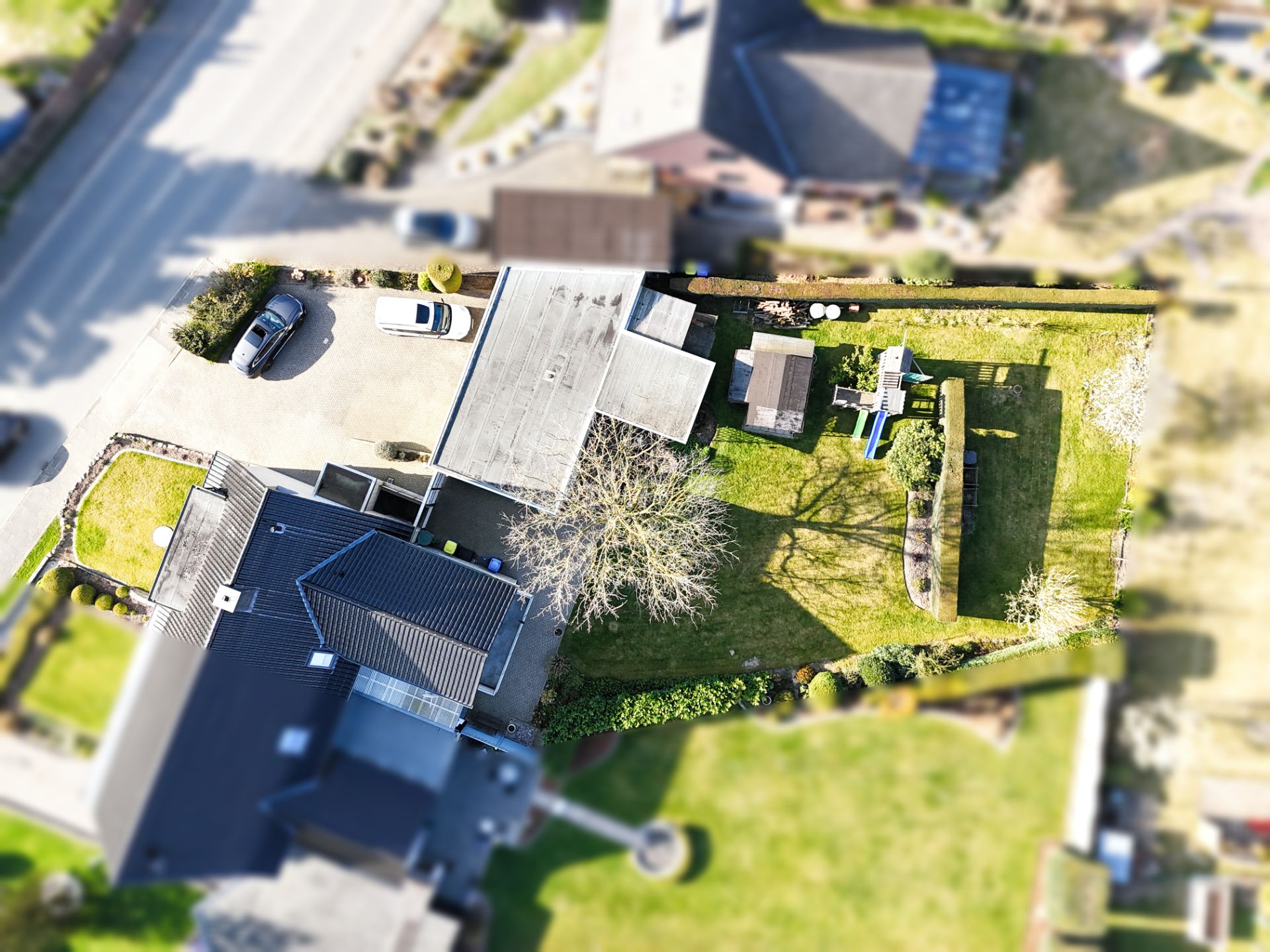 Luftaufnahme eines Wohnhauses mit Garten, Garage, zwei geparkten Autos und Rasenfläche.