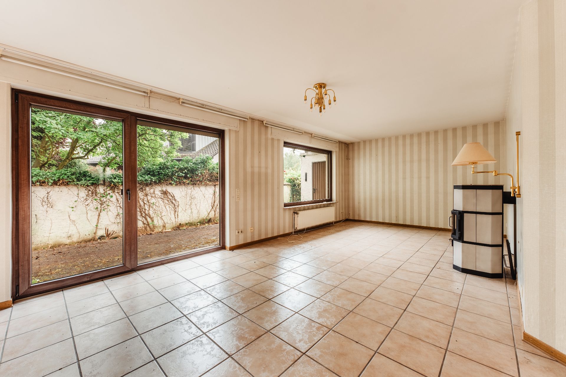 Helles Wohnzimmer mit Fliesenboden, großen Fenstern und einer Stehlampe in der Ecke.