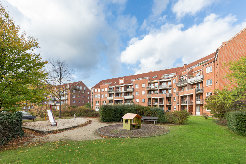 Mehrfamilienhaus mit Spielplatz, Rutsche und Spielhaus im begrünten Innenhof.