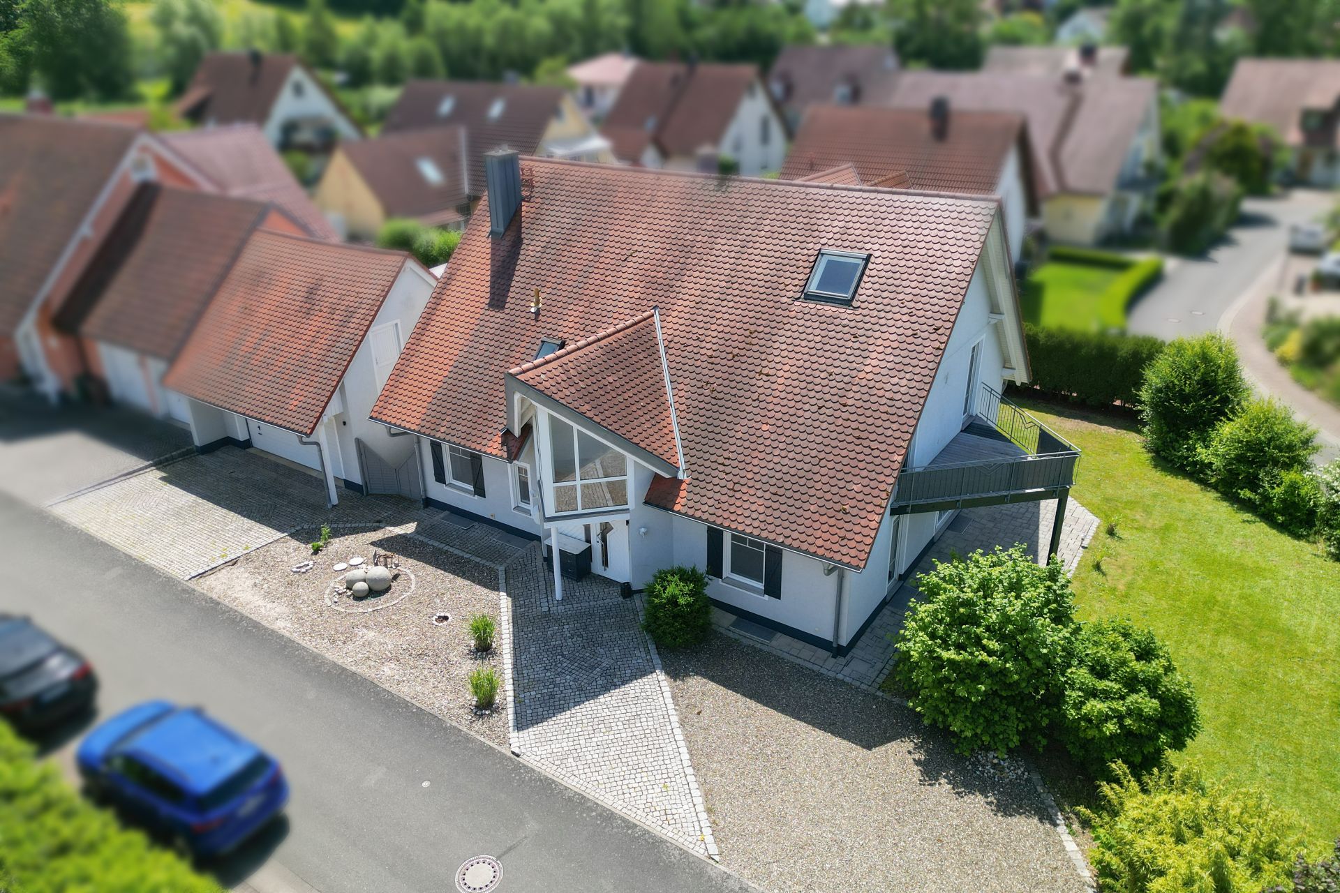 Einfamilienhaus mit rotem Dach, Einfahrt und kleinem Garten, aus der Vogelperspektive aufgenommen.