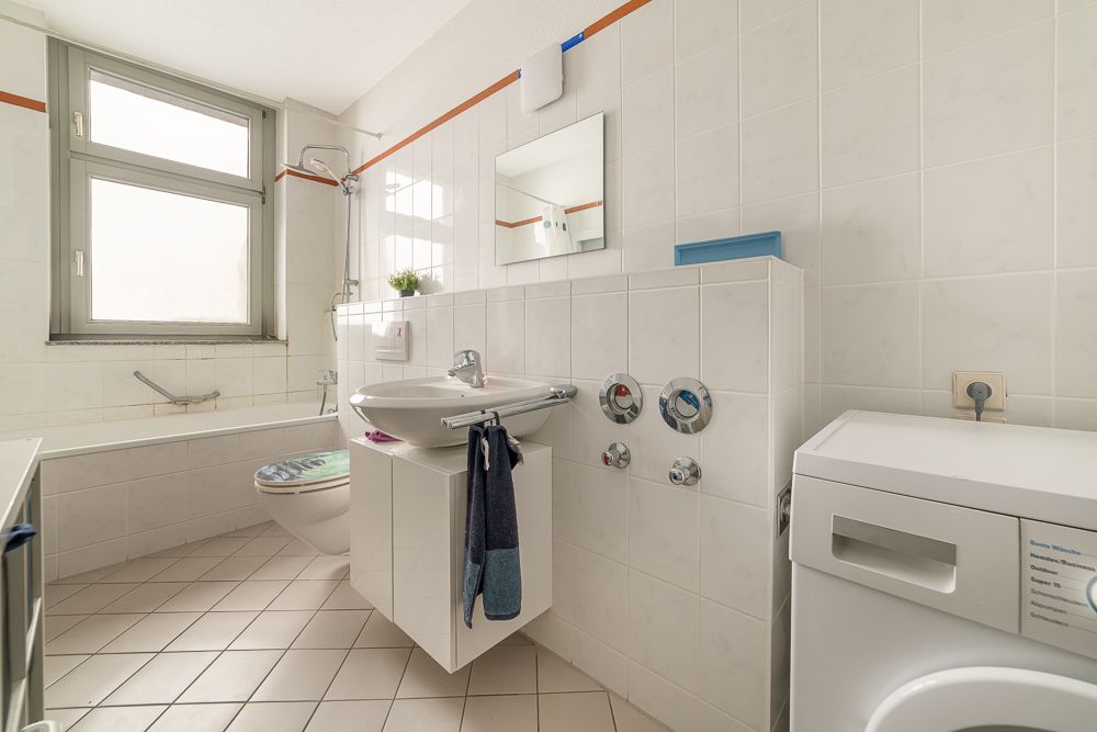 Helles Badezimmer mit Badewanne, Waschbecken, Toilette, Spiegel und Waschmaschine.