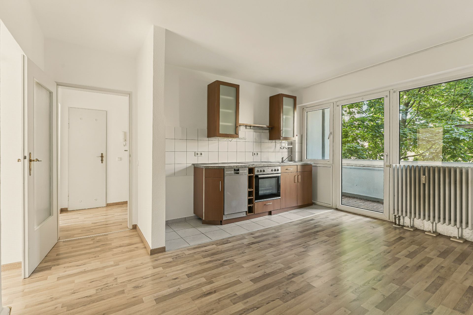 Helle Küche mit Herd, Spüle und Zugang zu einem Balkon, Parkettboden und großen Fenstern.