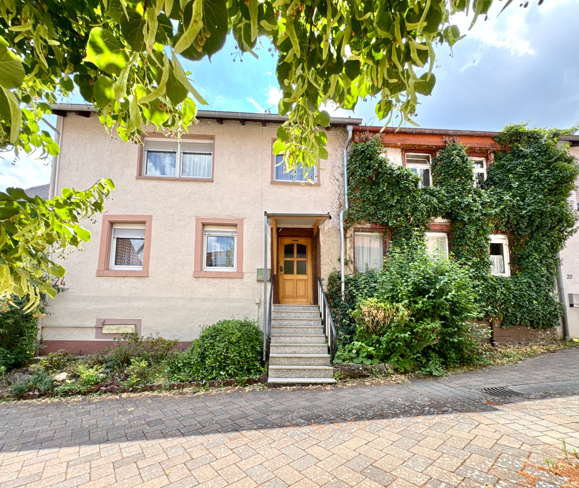 Zweistöckiges Wohnhaus mit Treppe zum Eingang, umgeben von Büschen und Pflanzen.