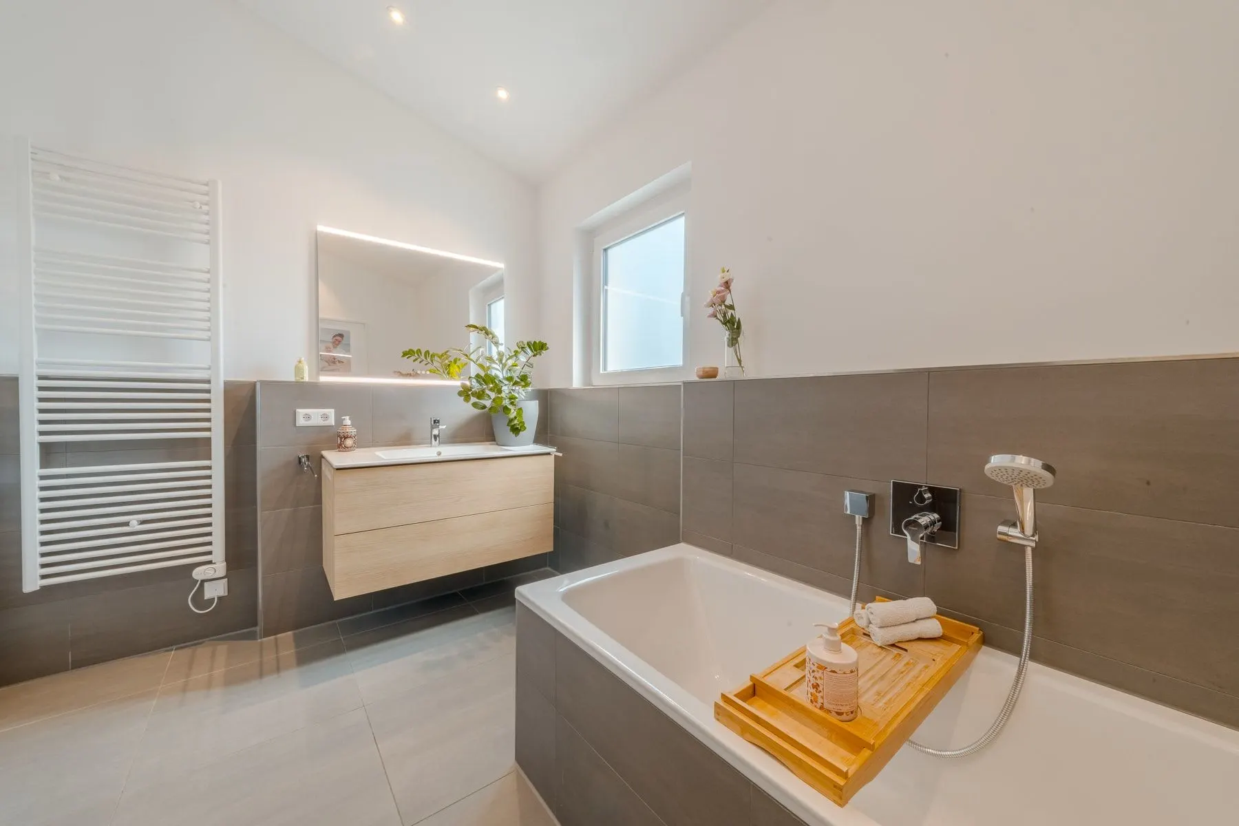 Modernes Badezimmer mit Badewanne, großem Spiegel, Waschbecken und Wandheizkörper.