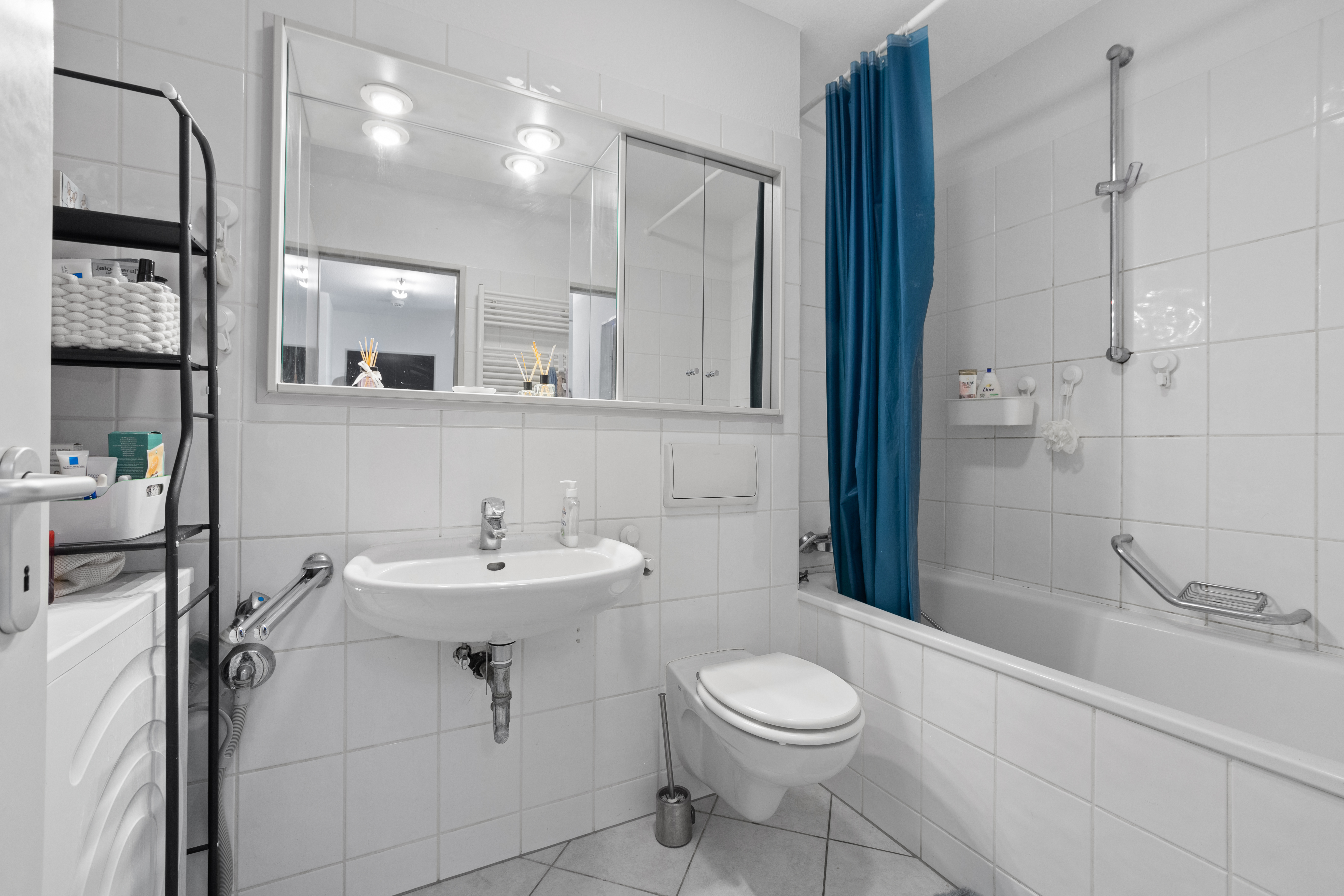Modernes Badezimmer mit Badewanne, blauem Duschvorhang, Waschbecken und Regal.