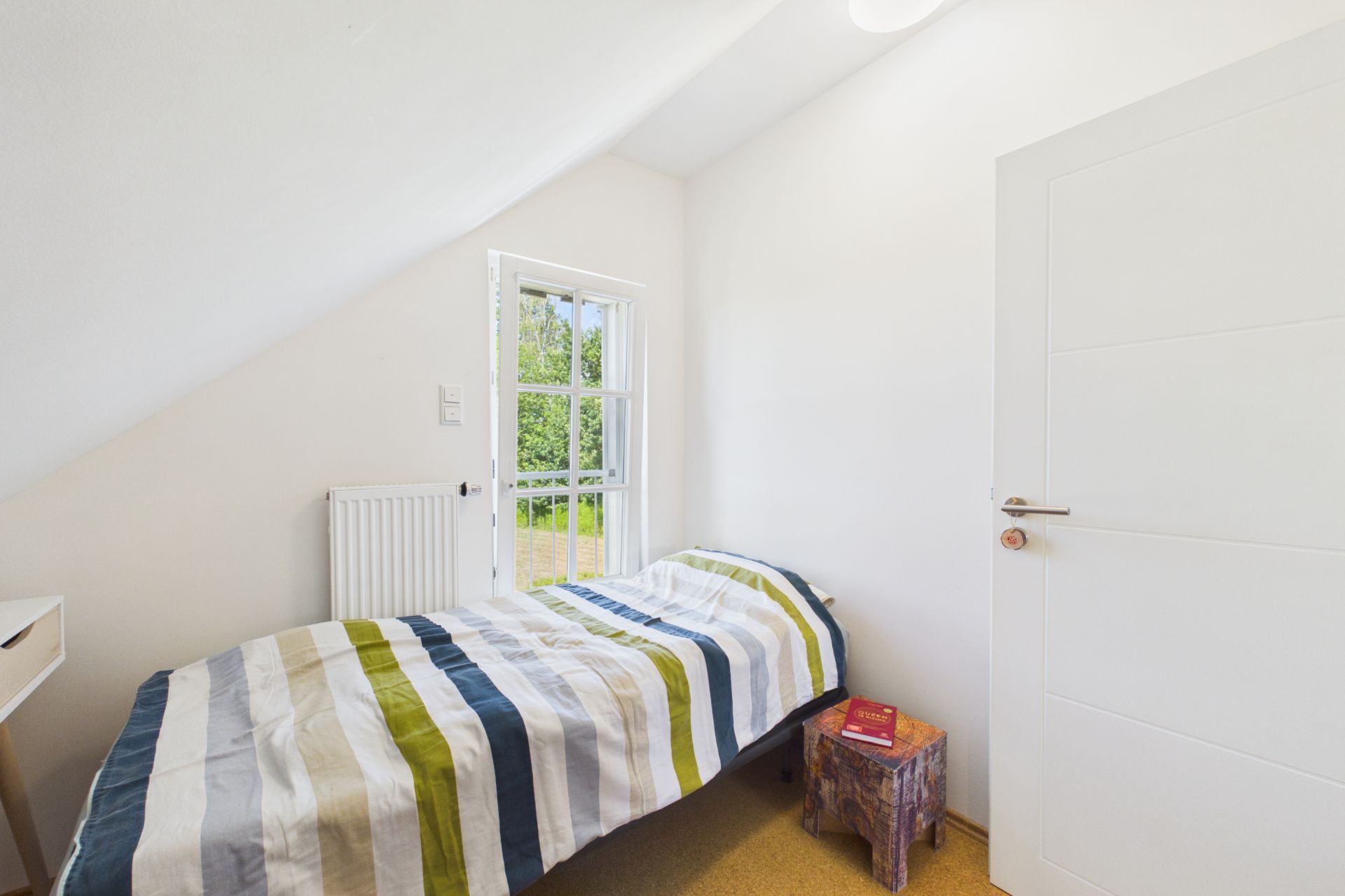 Kleines Schlafzimmer mit Einzelbett, gestreifter Bettwäsche, einem Fenster und einem kleinen Nachttisch.