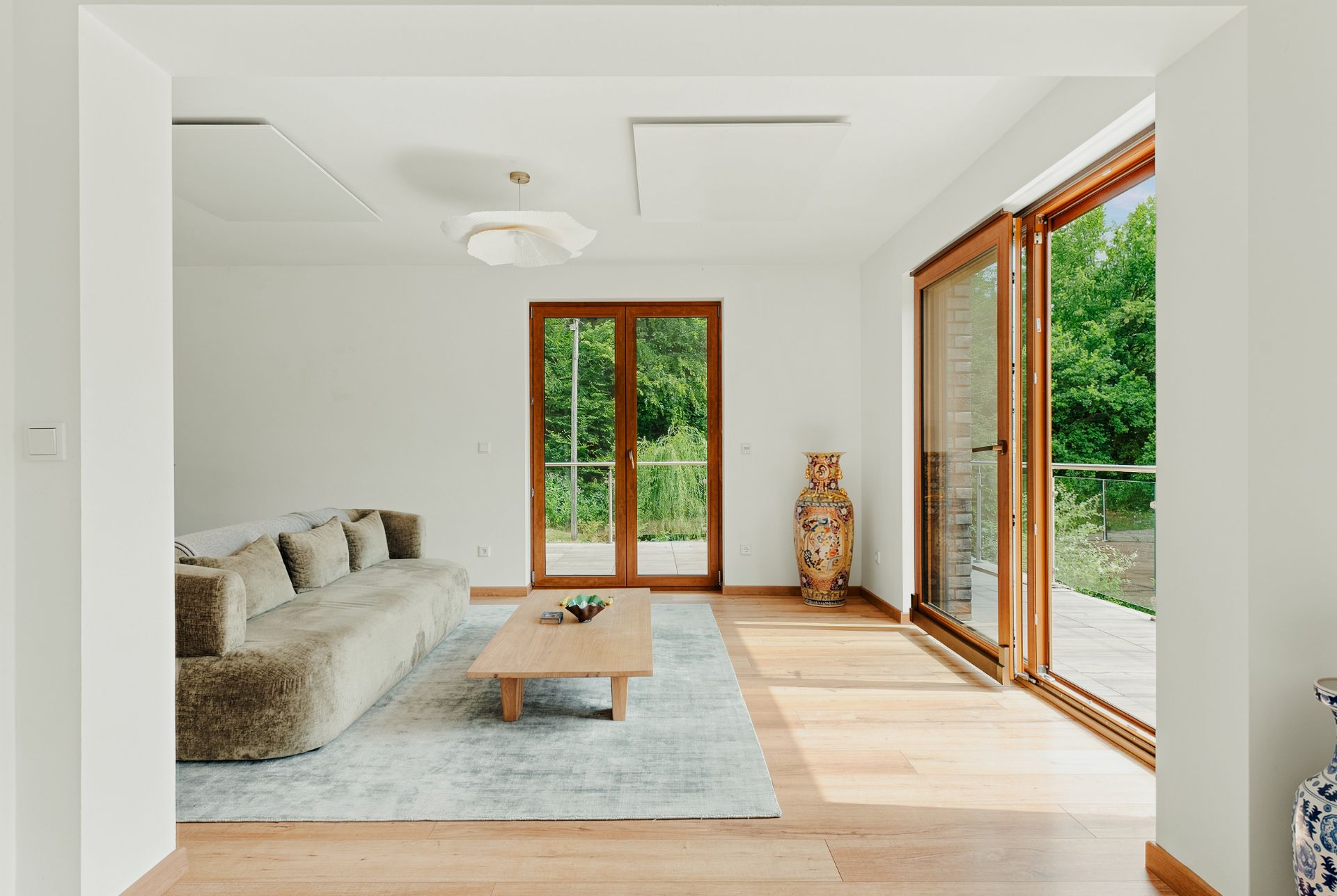 Helles Wohnzimmer mit großem Sofa, Holztisch, Teppich und Zugang zur Terrasse durch große Glastüren.