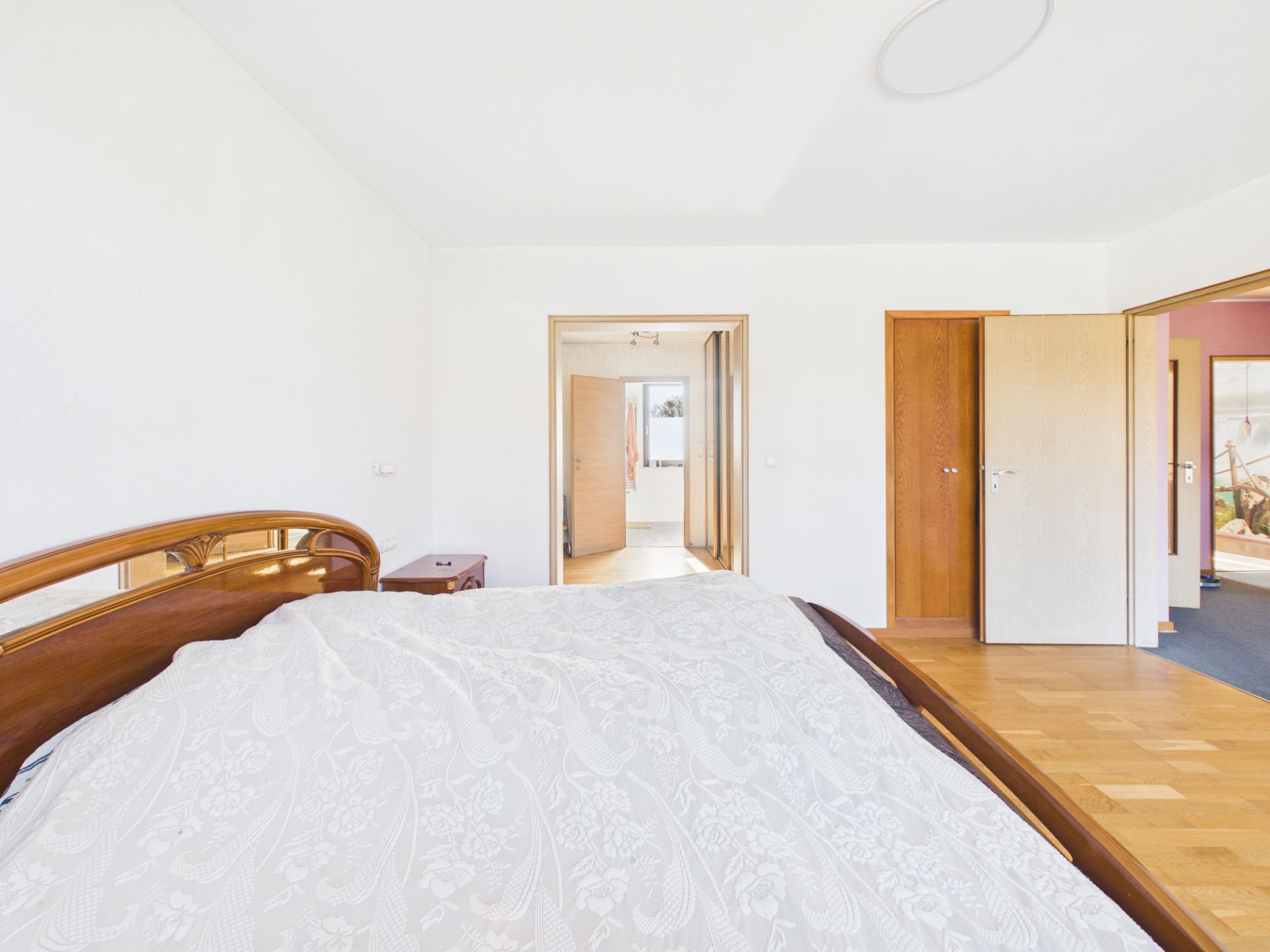 Helles Schlafzimmer mit Holzbett, Nachttisch und mehreren offenen Türen zu anderen Räumen.