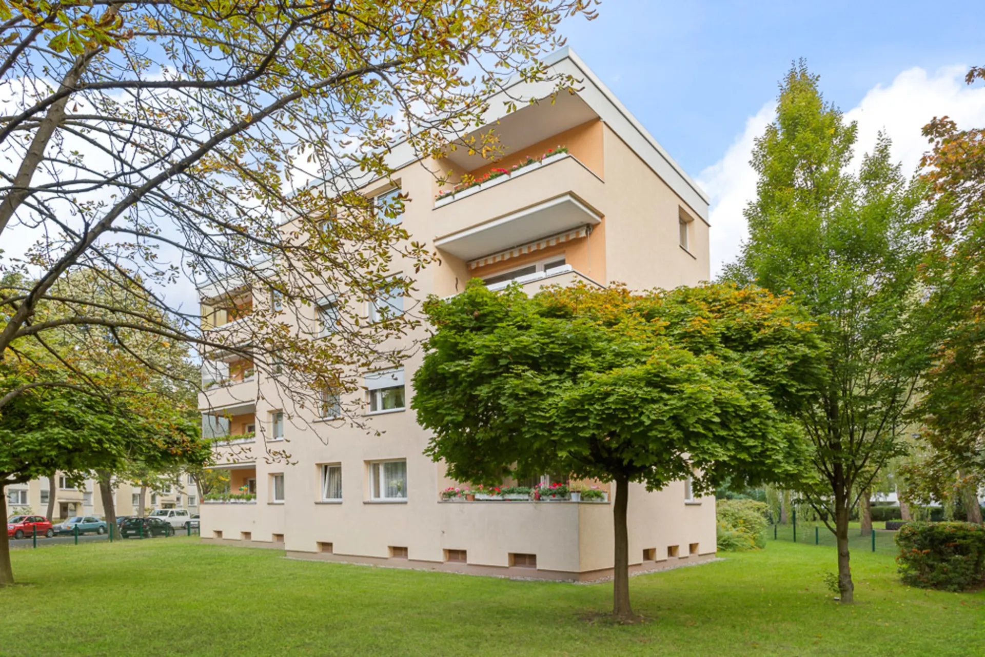 Mehrfamilienhaus mit Balkonen und umgebenden Bäumen auf einer begrünten Wiese.
