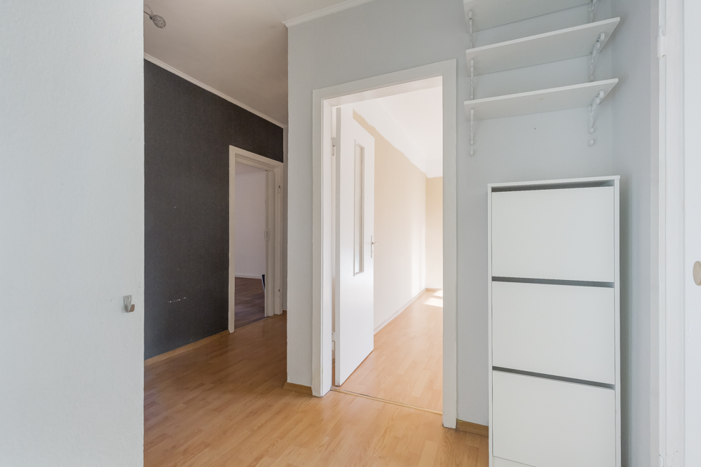 Heller Flur mit Holzfußboden, weißem Regal und offenen Türen zu weiteren Zimmern.
