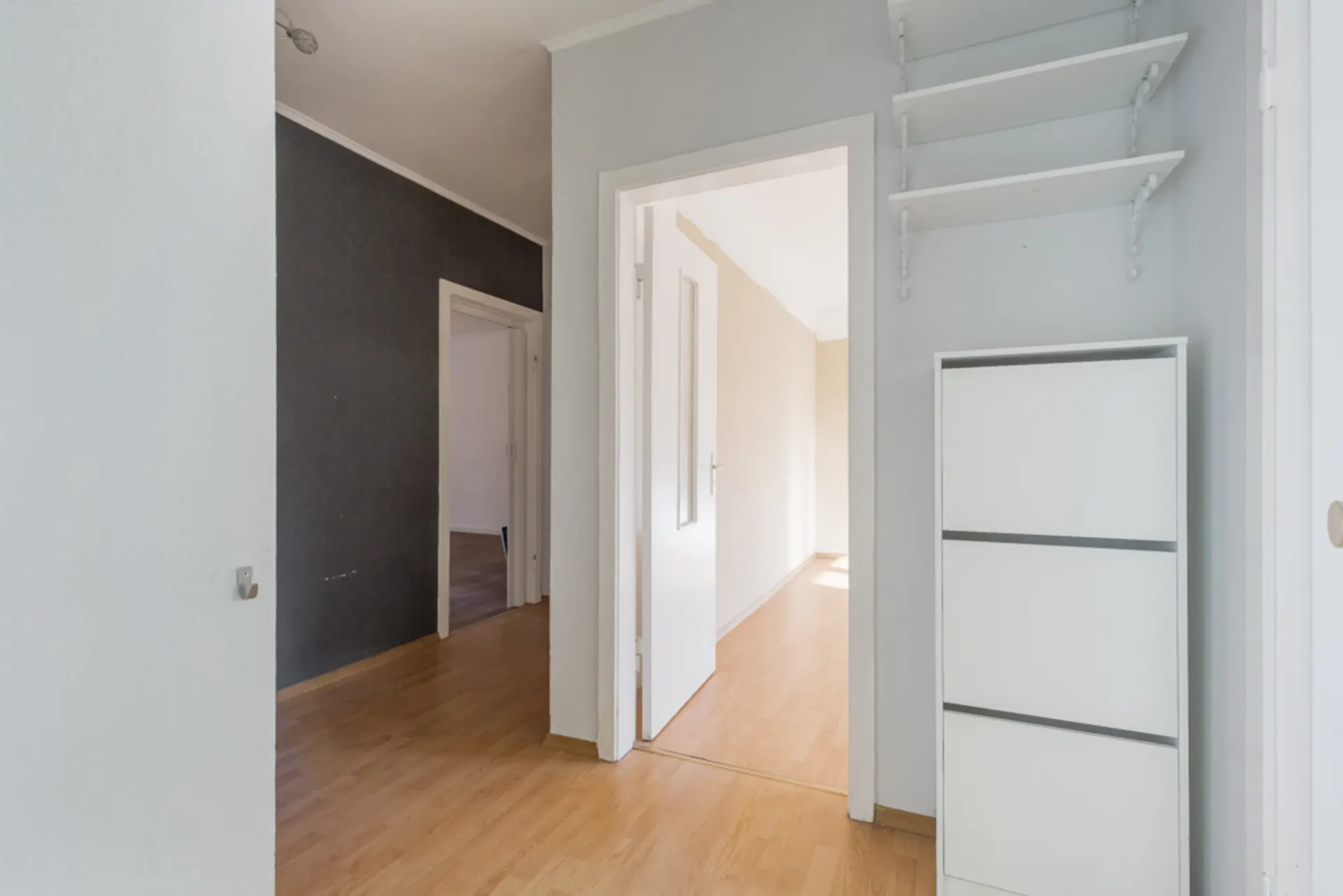 Heller Flur mit Holzfußboden, weißem Regal und offenen Türen zu weiteren Zimmern.