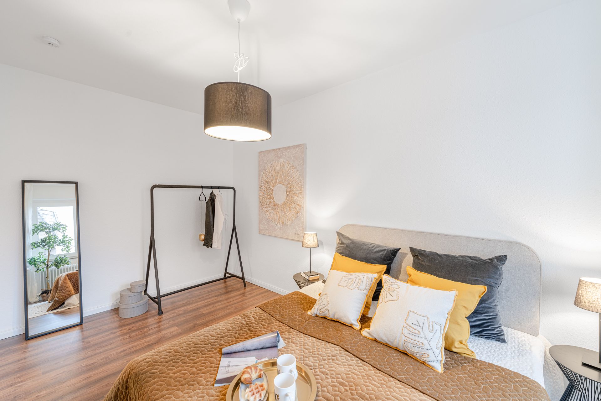 Helles Schlafzimmer mit Doppelbett, Spiegel, Kleiderständer und Holzboden.