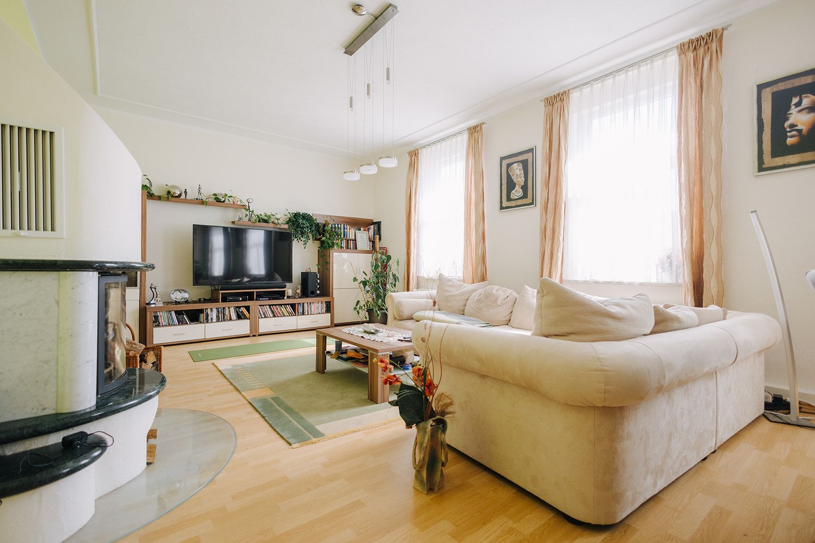 Helles Wohnzimmer mit beigem Sofa, großem Fernseher, Teppich und Pflanzen.