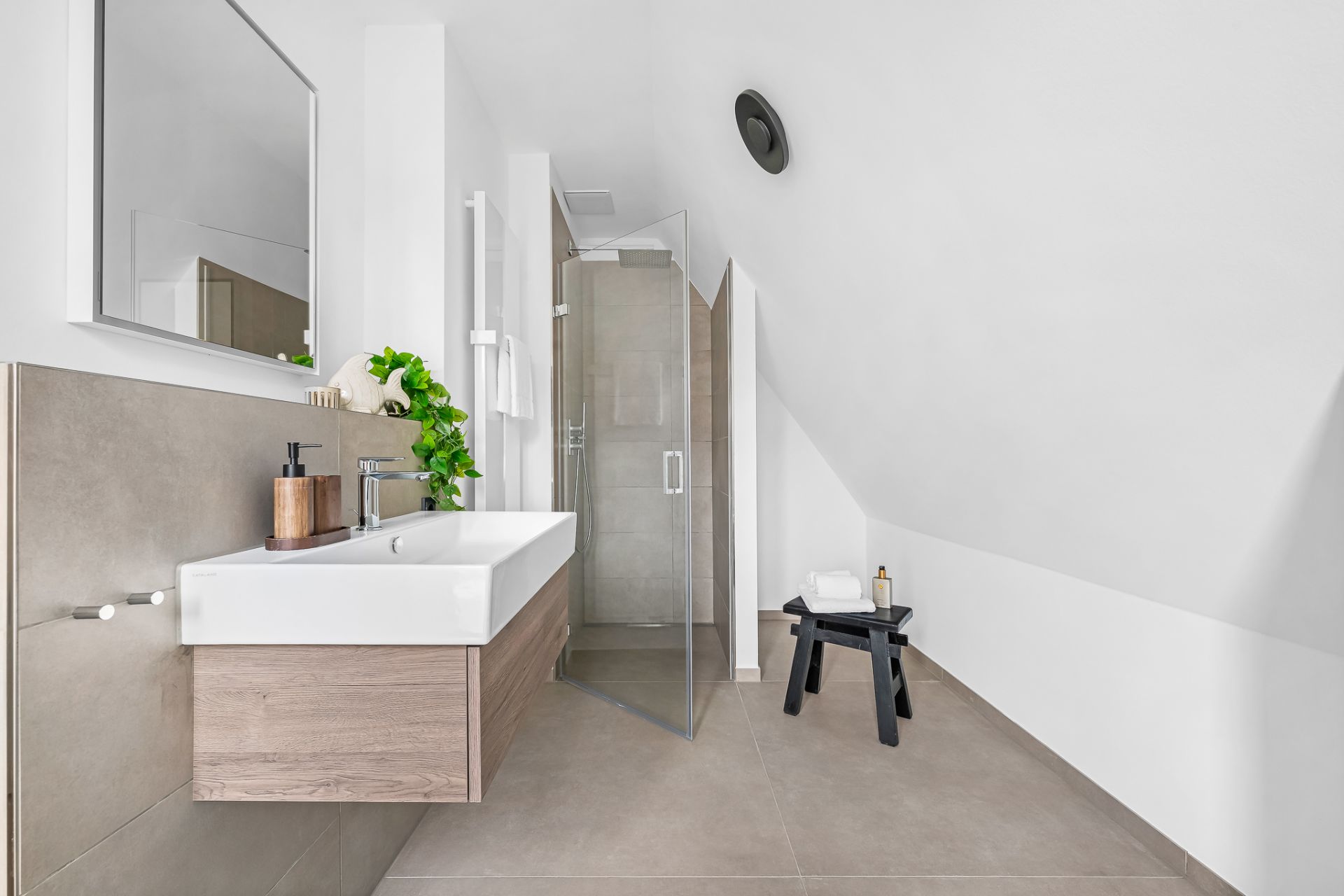 Modernes Badezimmer mit großem Waschbecken, offener Dusche und einem kleinen schwarzen Hocker.