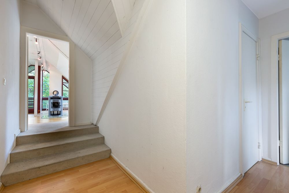Heller Flur mit Holzfußboden, Treppe und Blick in ein Wohnzimmer mit großen Fenstern.